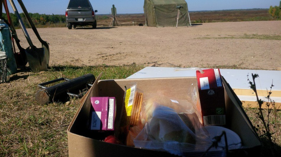 Box with juiceboxes and crackers on background of field, truck, and tent